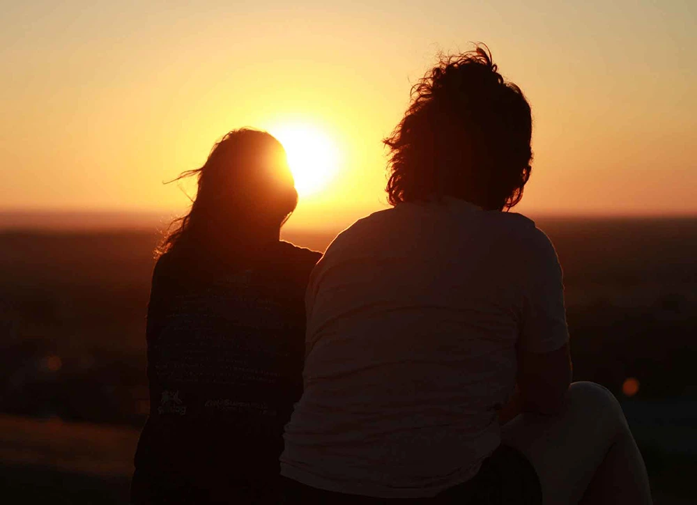 A silhouette of two people at sunset