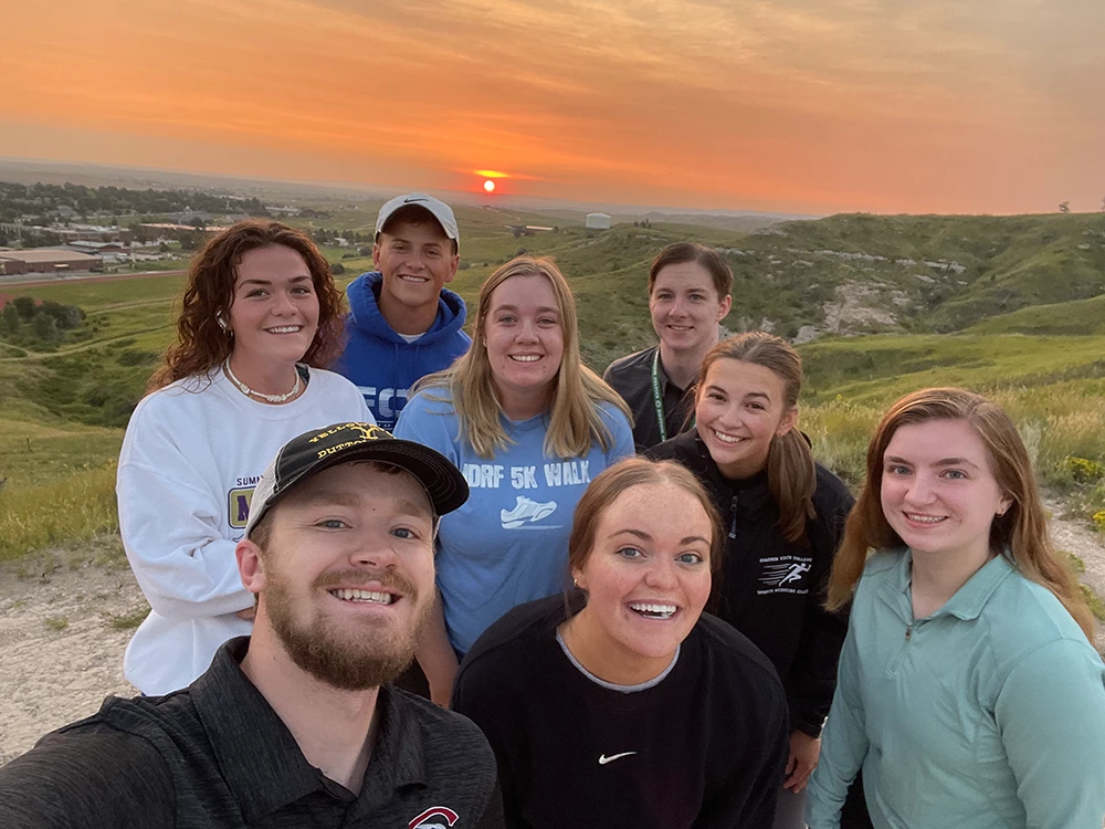 A group of students smiling at the camera at sunrise
