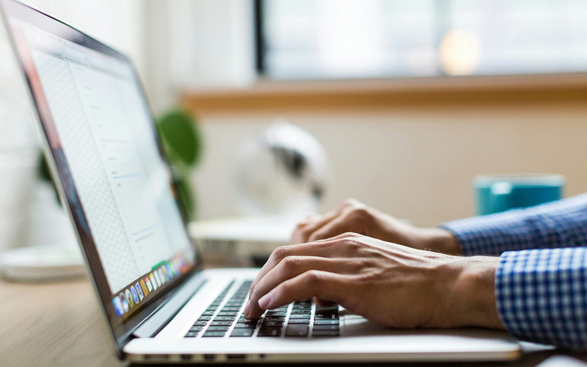 Close of photo of a laptop with a pair of hands using it