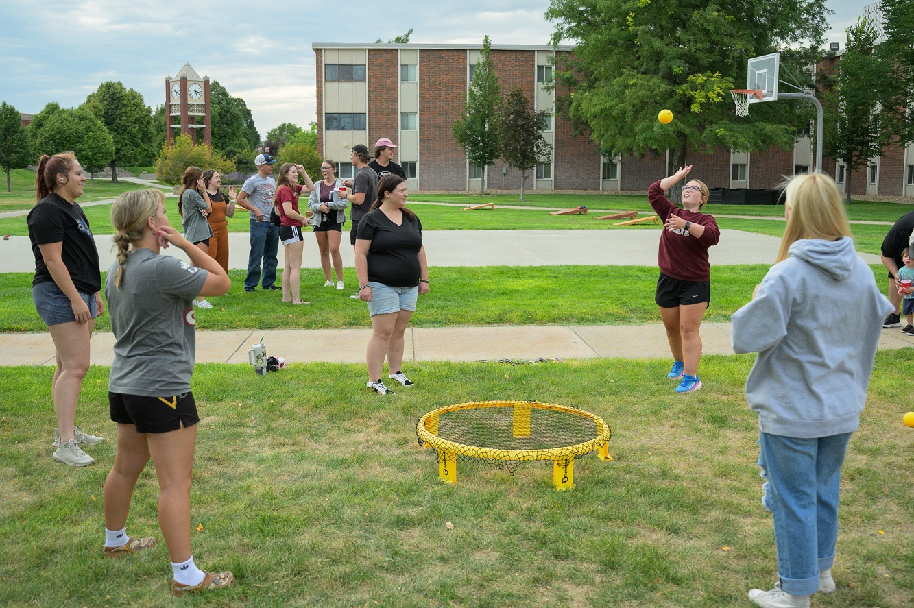 The image is of students tossing a ball at one another in an outdoor setting.