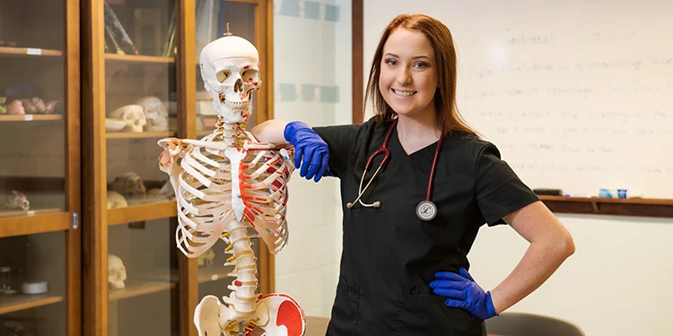 Woman in scrubs with stethoscope next to a skeleton