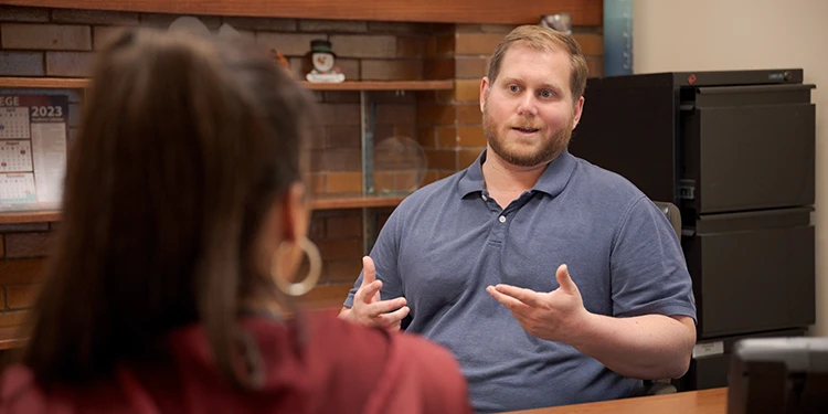 Two people discussing something. The image is a closeup of the back of a woman's shoulder while she talks to a man