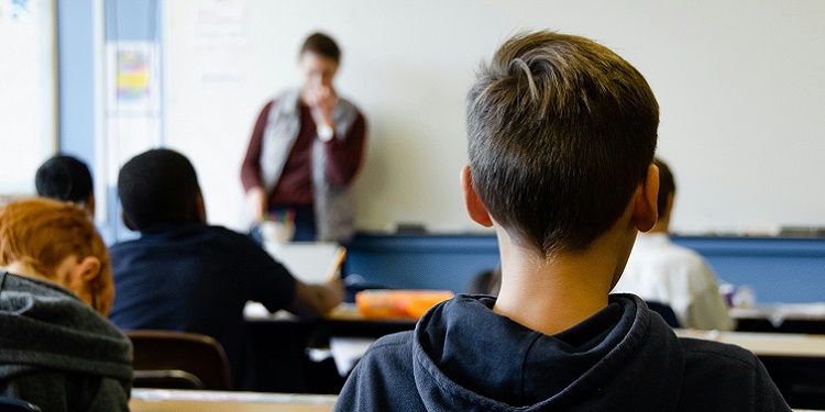 The back of a child's head in a classroom, with the teacher at the front of class