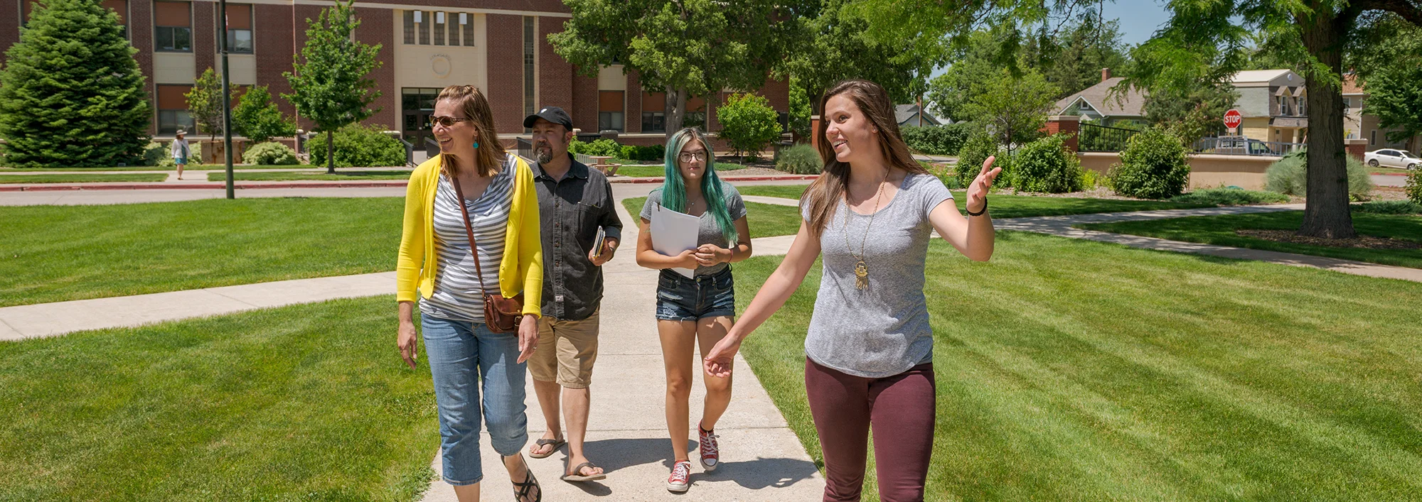 Student tour guide leading a family across a campus green space