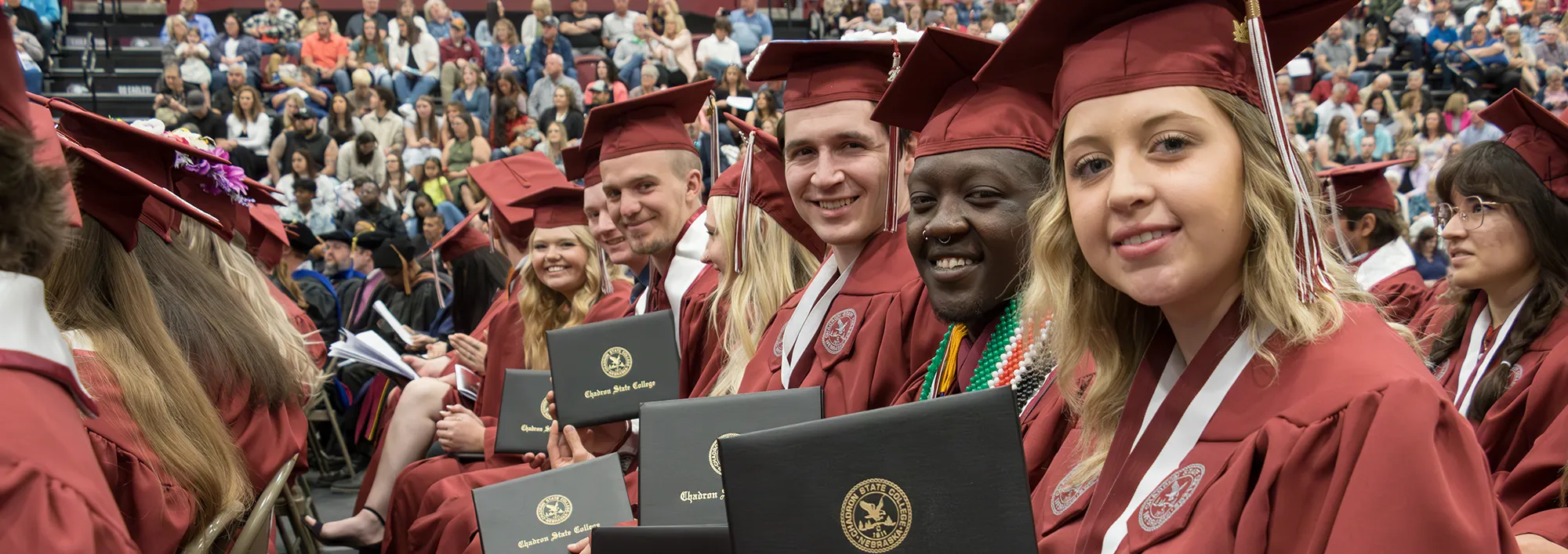 Several students wearing graduation regalia and holding their diplomas