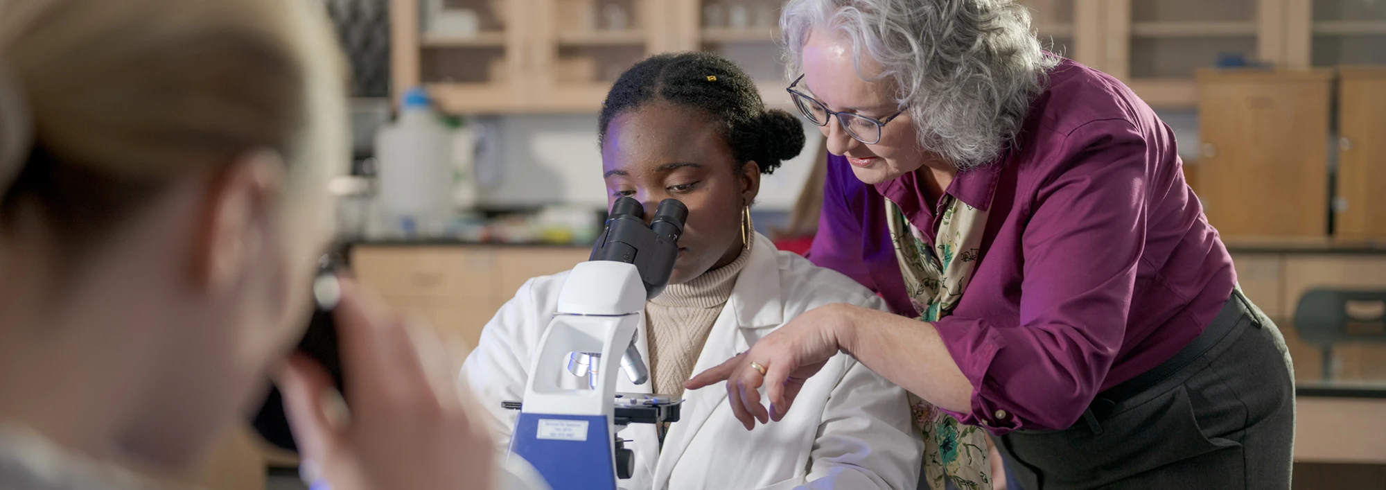 A biology professor showing a student details of a slide under a microscope