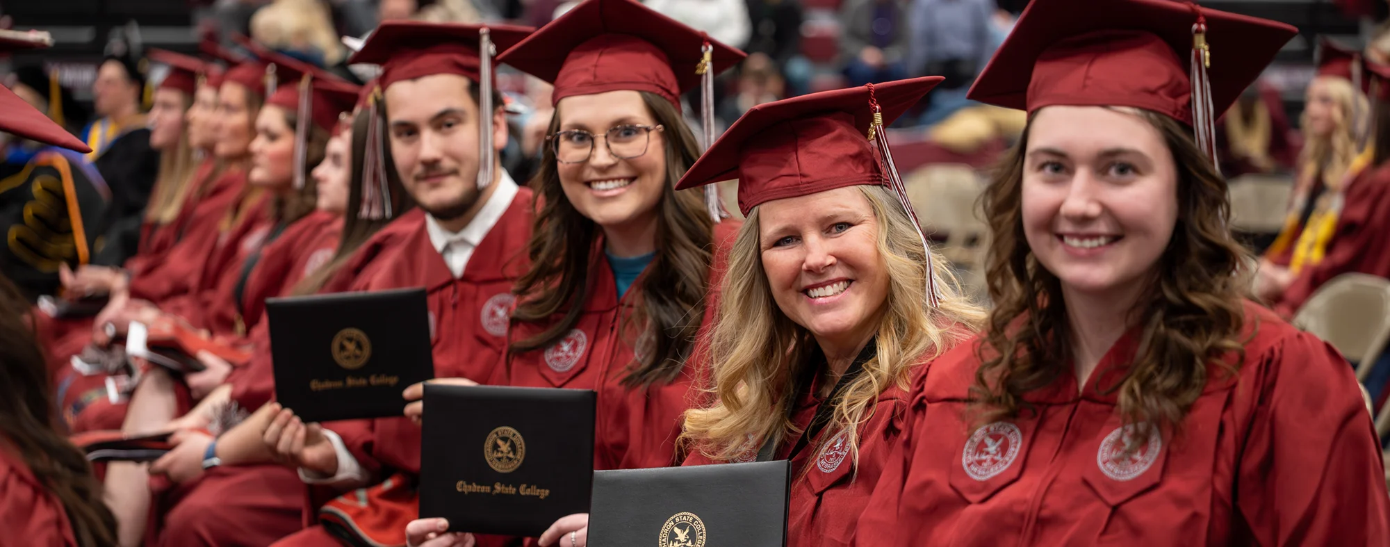 Group of Chadron State College graduates in regalia holding their diploma covers and smiling