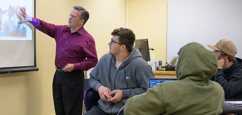 A teacher gestures toward a projected image during a business class
