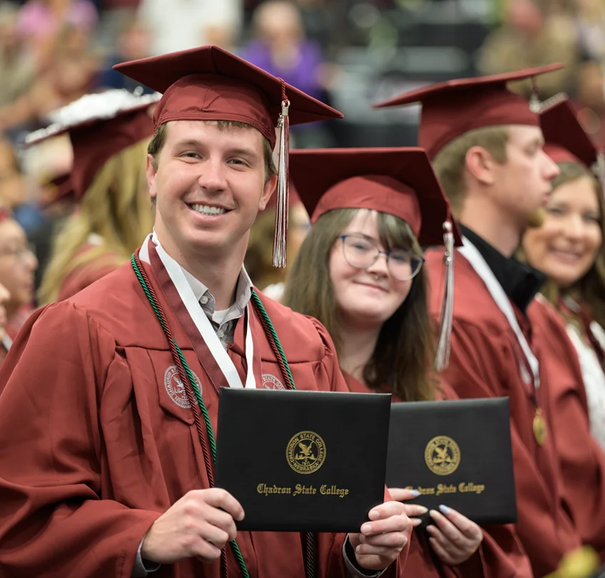 Several students holding their diplomas and smiling during graduation