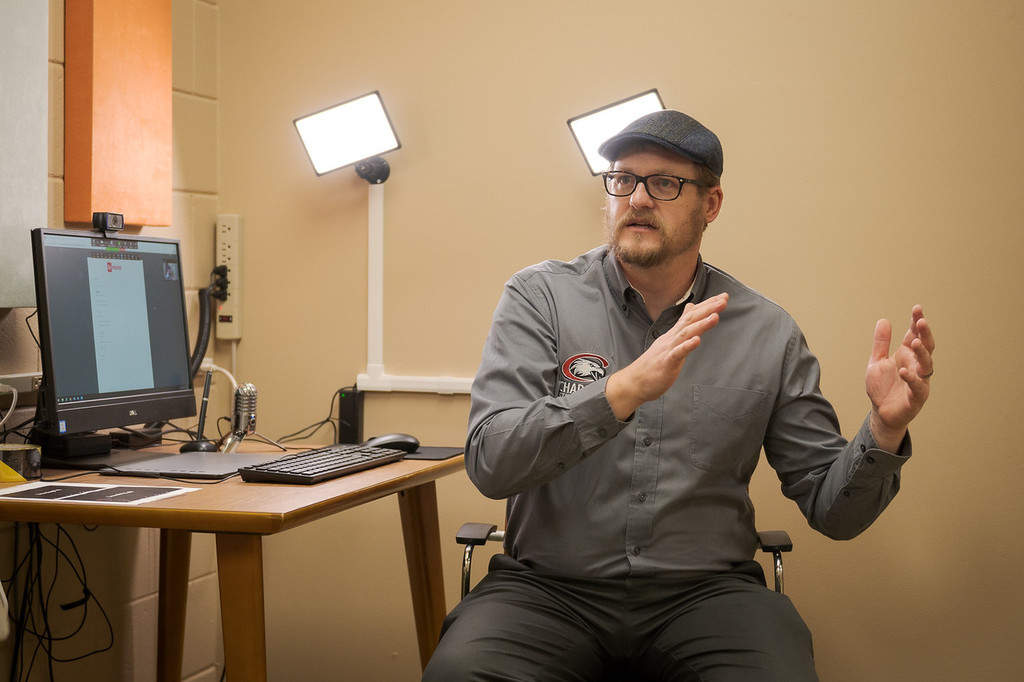 Tom Tylee, director of the Office of Academic Success, describes how technology can be used to help students. Tylee sits at a system used for remote learning assistance, which includes a video conferencing application, lighting, microphone, and green screen background.