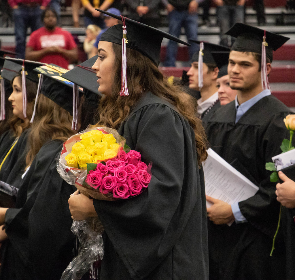 A CSC graduate stands holding flowers during the commencement ceremony.
