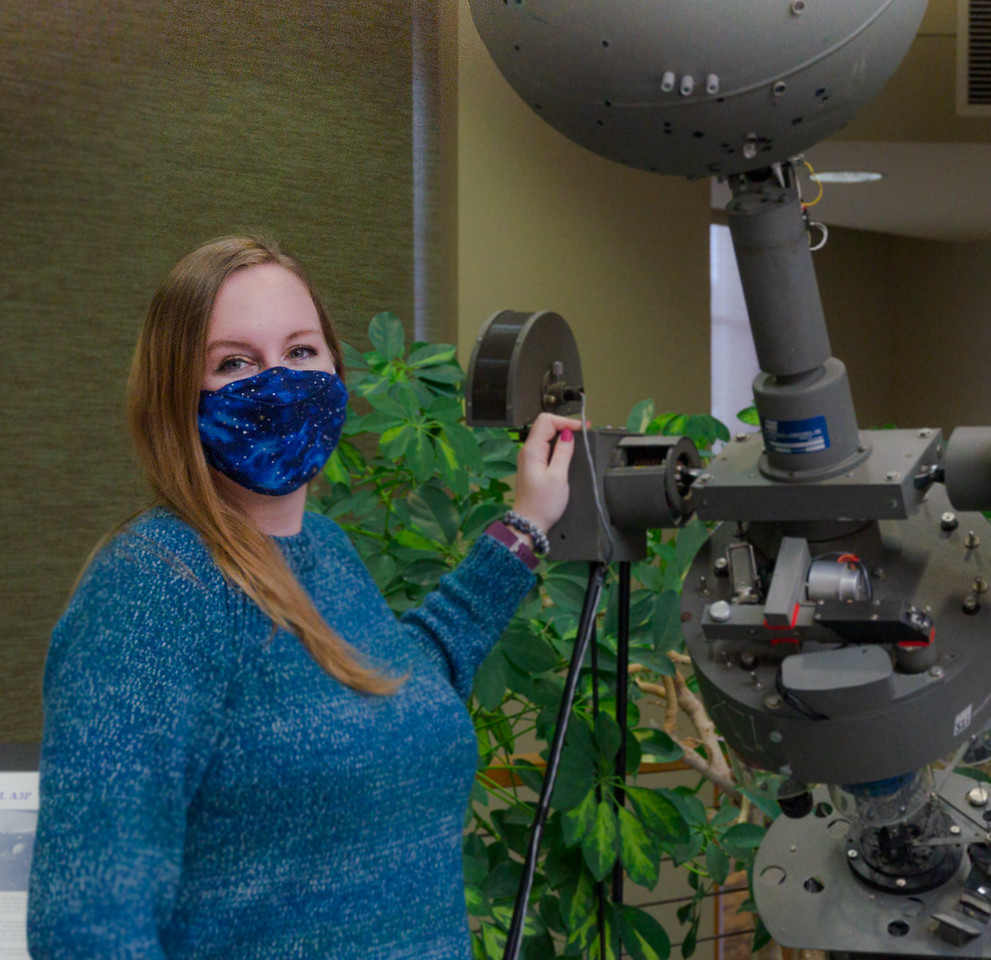 Dr. Tawny Tibbits stands next to the retired optical mechanical projection ball on display in the Mari Sandoz High Plains Heritage Center