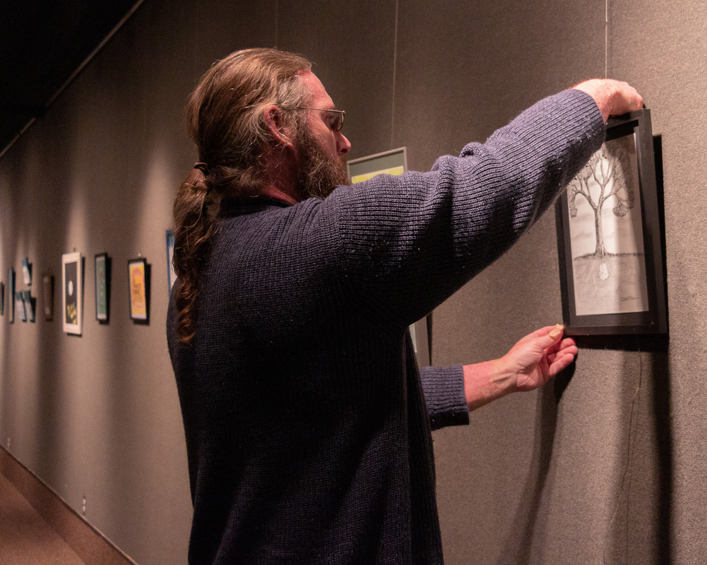 Matthew D. Reese, youth transition worker with Cirrus House, prepares the exhibit in Memorial Hall's Main Gallery.