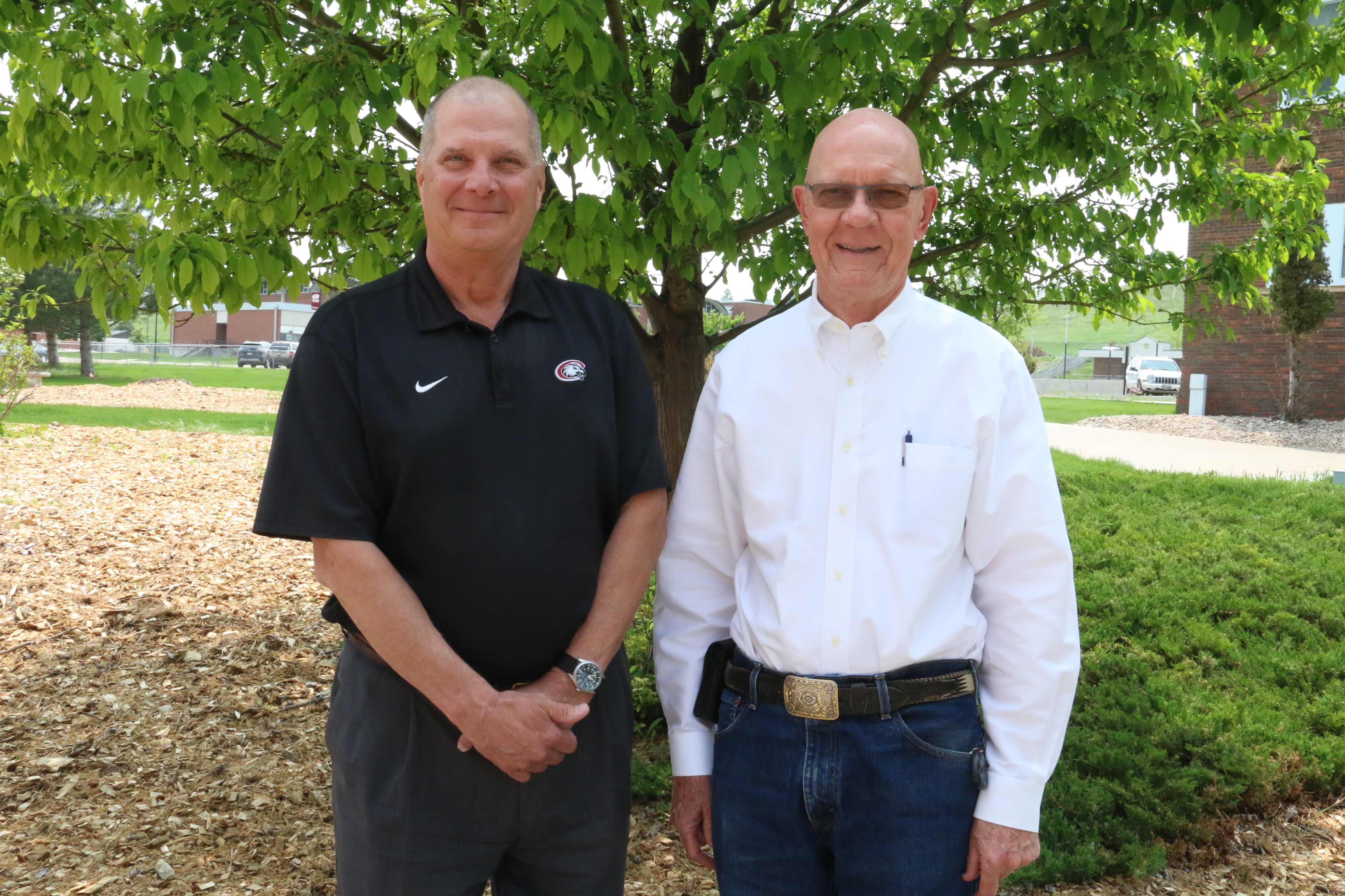 Two men pose outside by a tree