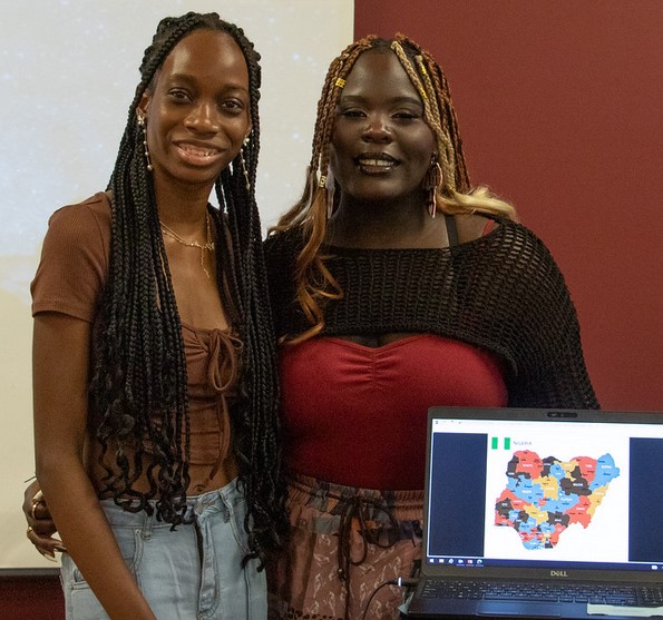 Two women posing by a laptop
