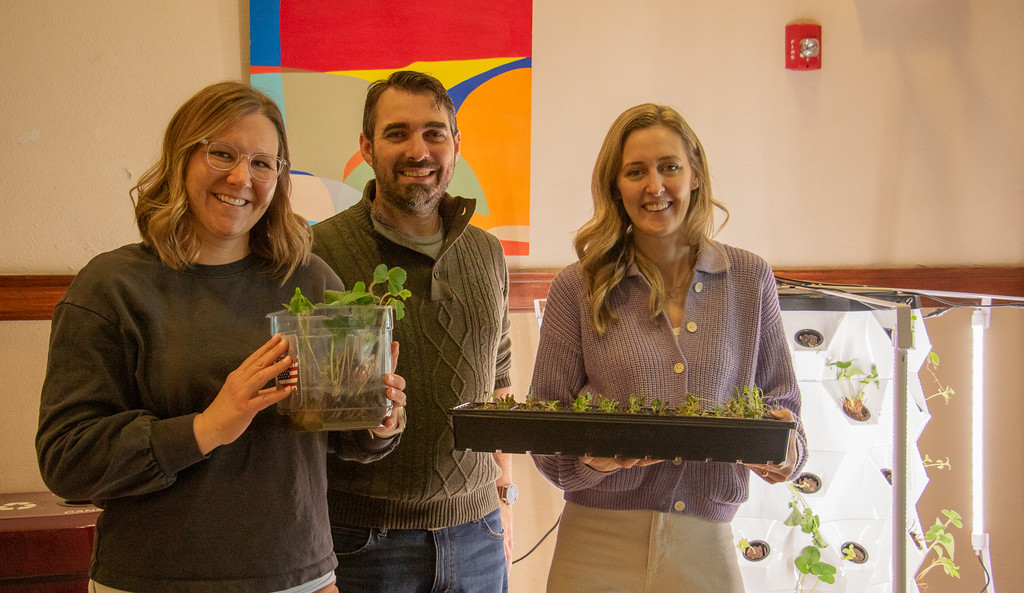 Three adults posing by an indoor plant tower