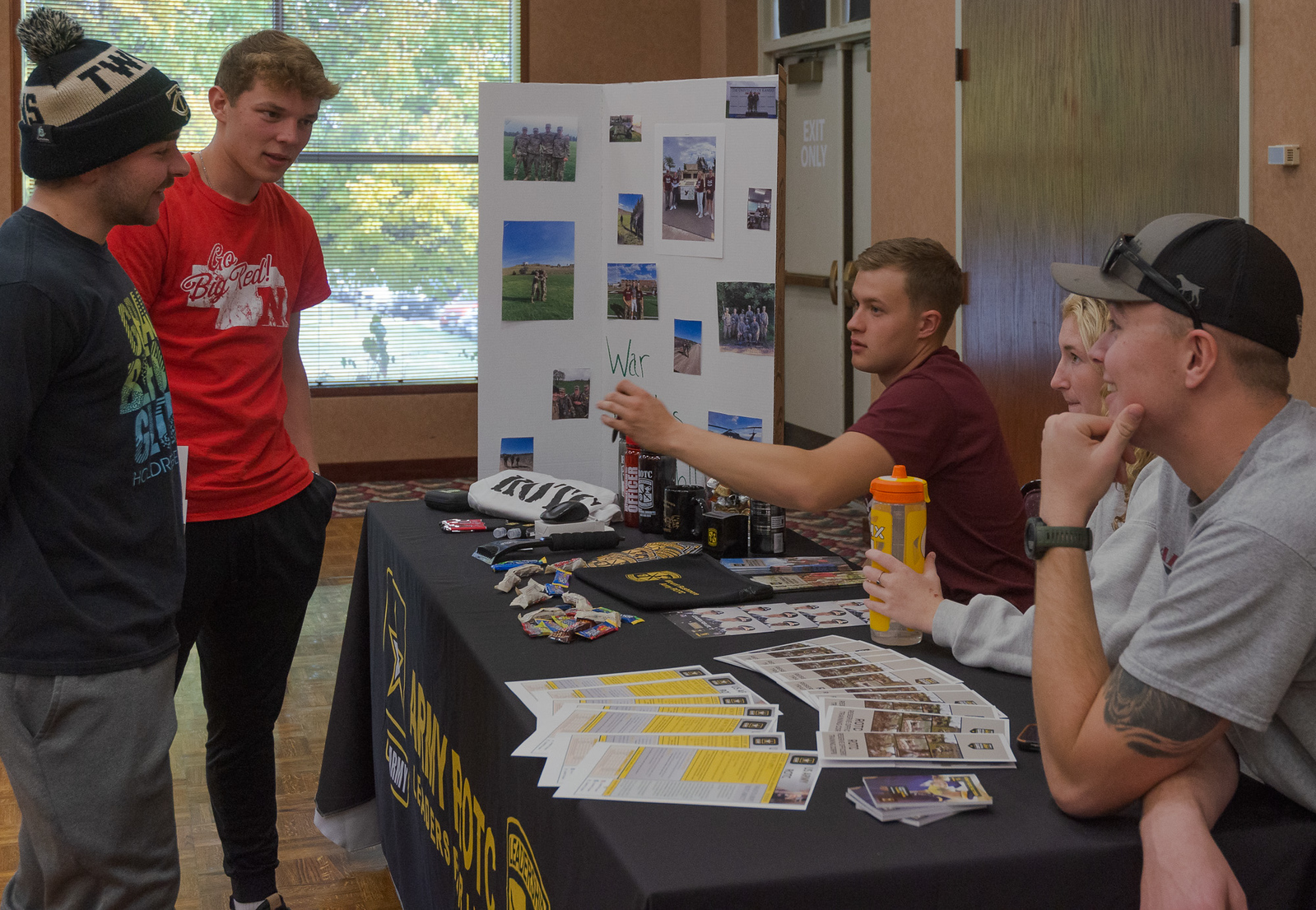Students sitting at a club fair booth speaking to standing students