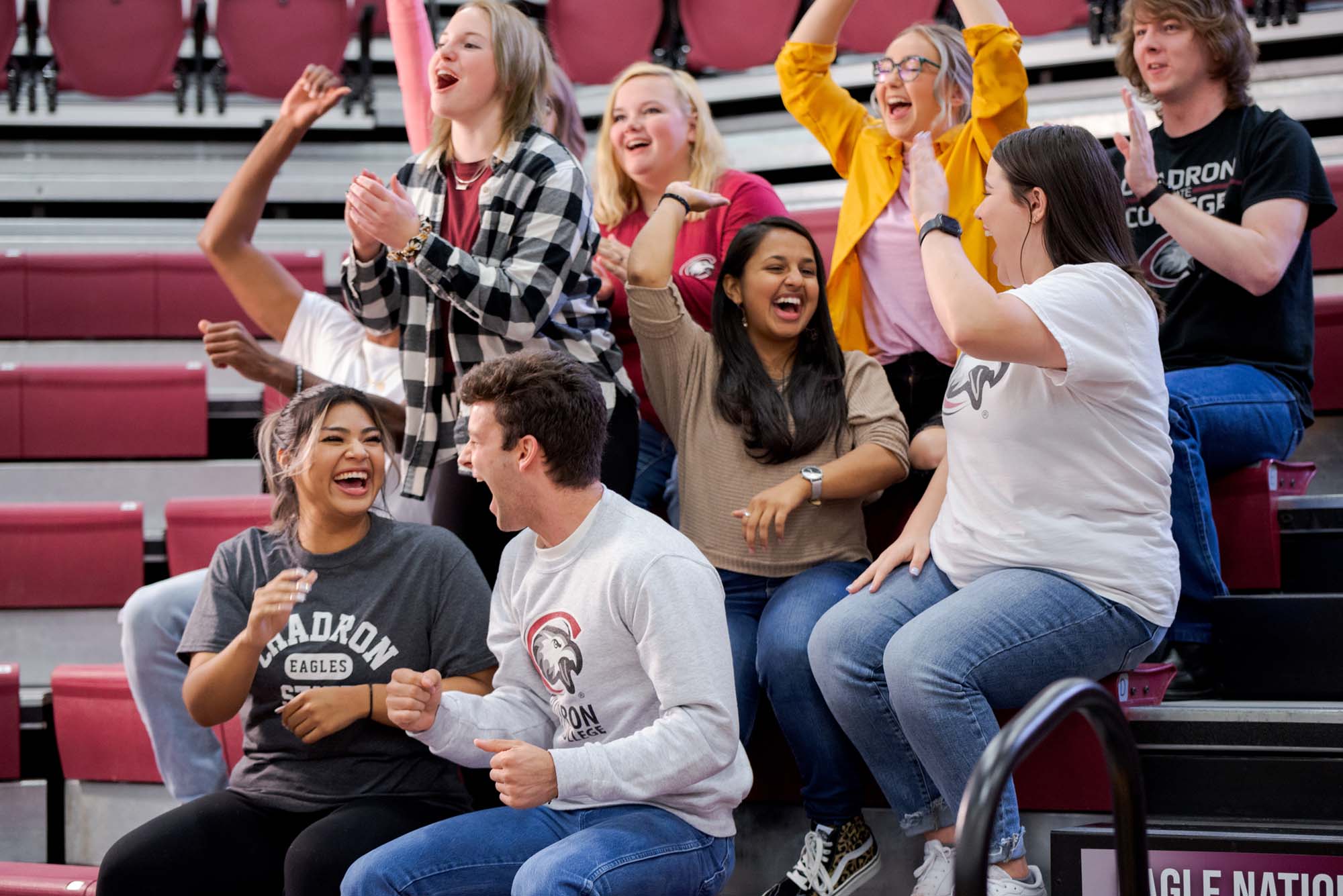 Students cheering while sitting in bleachers, at a sporting contest