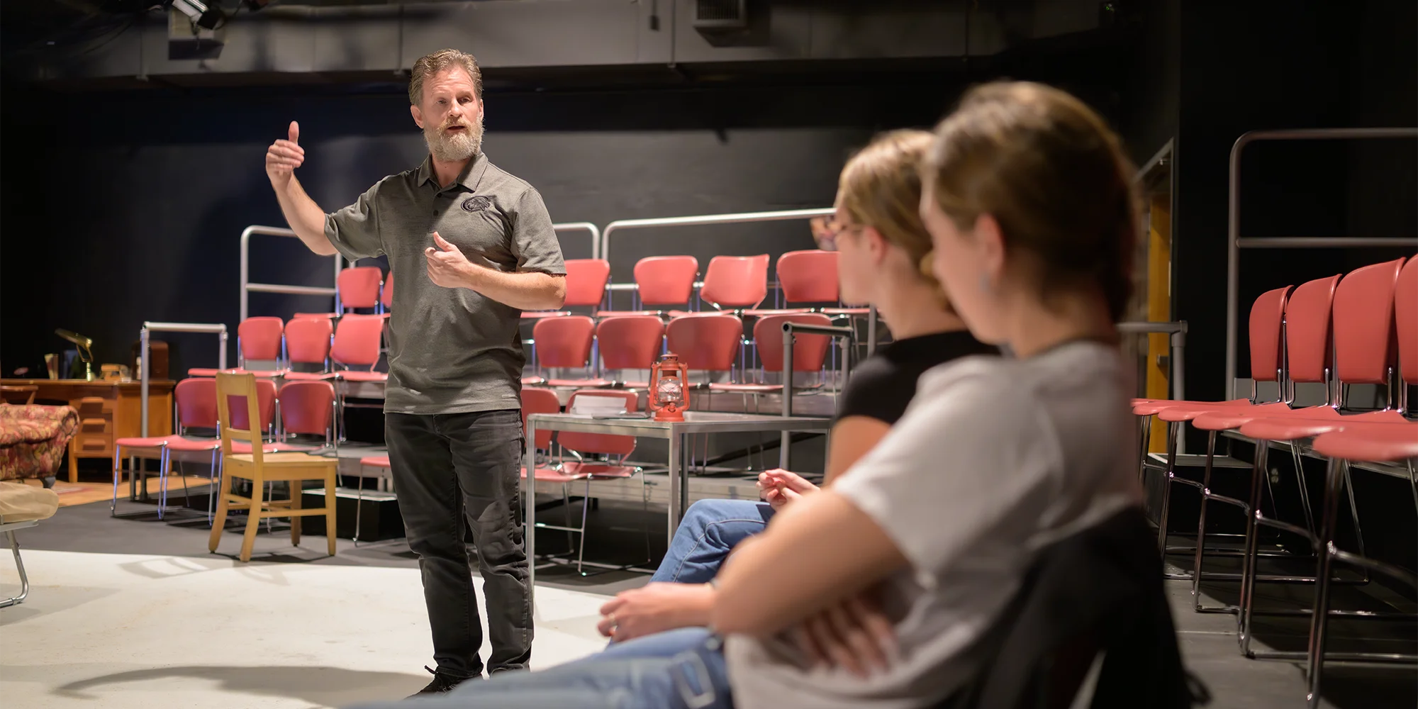 A theatre professor speaks to students at a black box stage