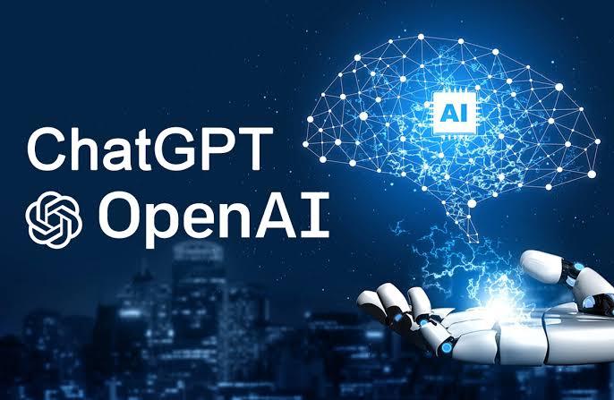 Blue and black city scape in the background. White lettering says ChatGPT and OpenAI. White flower circle logo for Open AI next to the words. In the right hand corner there is a white robot hand open. A  white digital brain is coming out of the hand. Inside the digital brain is what looks like a white computer chip. The center of the computer chip says AI.