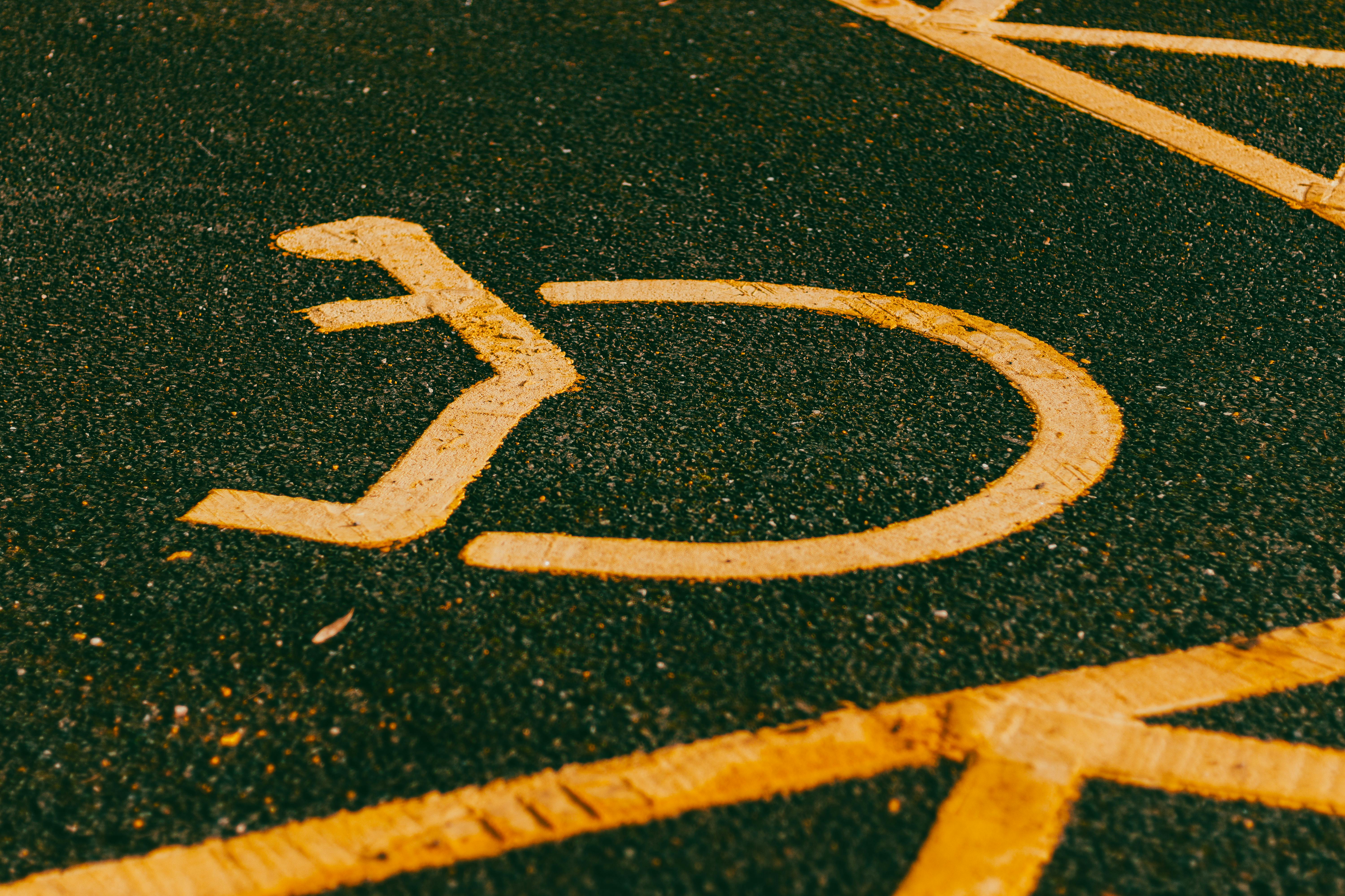 The International Symbol of Access painted in yellow on asphalt pavement.