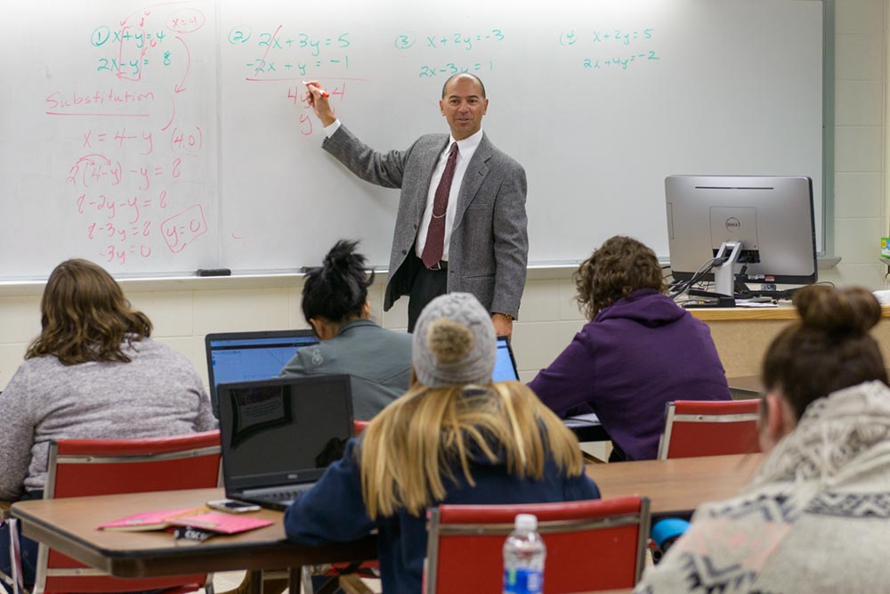 Math classroom scene with professor gesturing at equations on the whiteboard